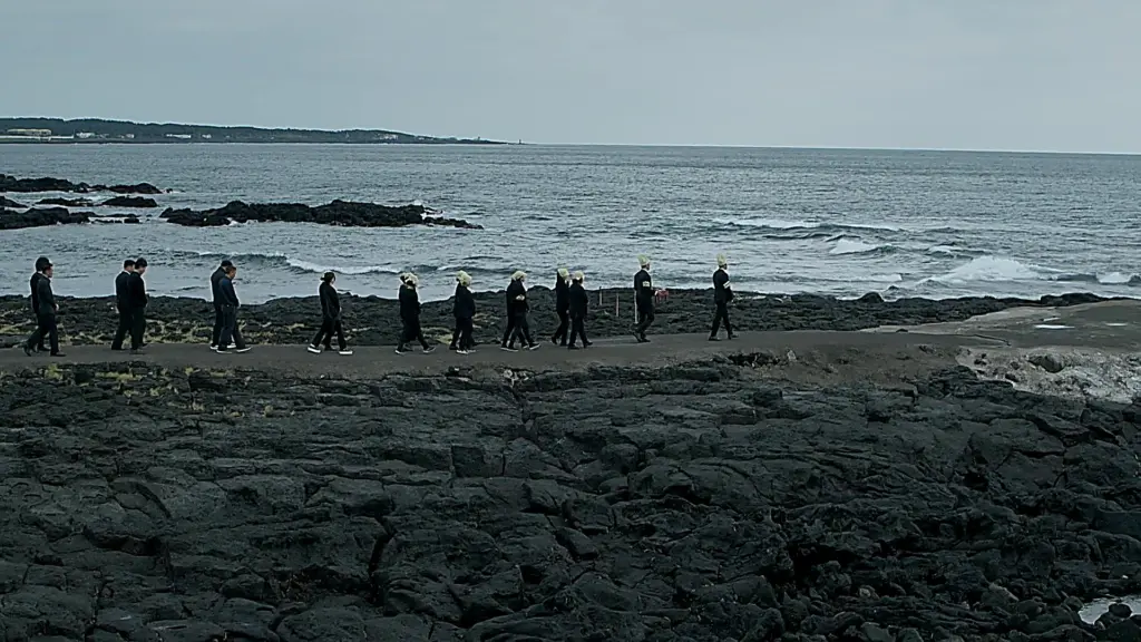 黒い玄武岩が広がる海岸の小道を一列になって歩く黒服の人々