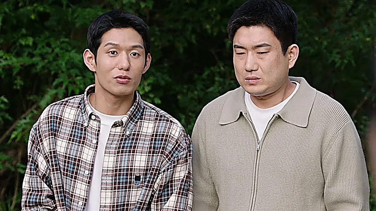 緑の木々を背景に並ぶチェック柄シャツの男性とベージュニットの男性