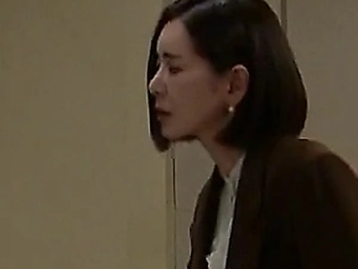 茶色のジャケット姿で扉の前に佇むショートボブの女性の横顔